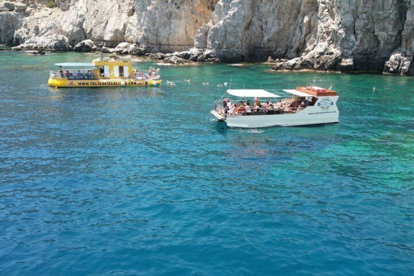 A white boat with people on it, a yellow boat, and rocky cliffs in the background. 5