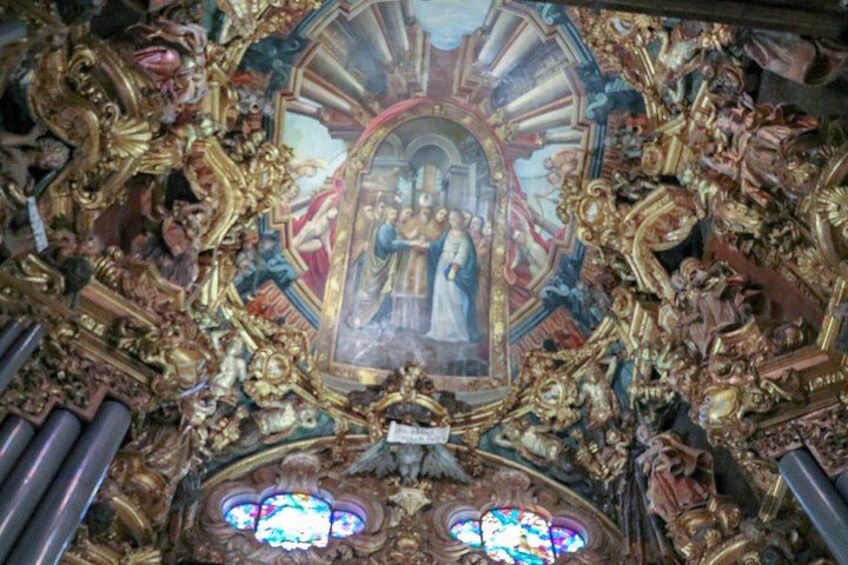 A detailed ceiling with ornate decorations, a central painting, and stained glass windows. 2