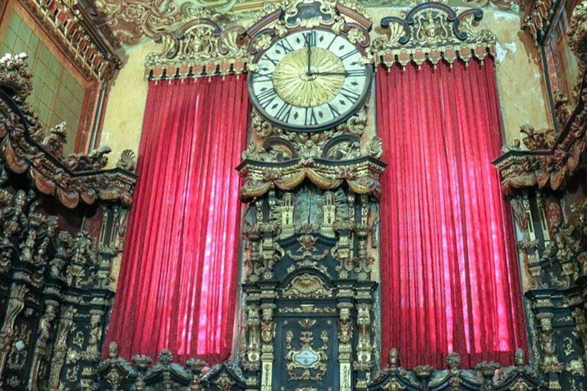 An ornate clock with Roman numerals, red curtains, and intricate architectural details. 3