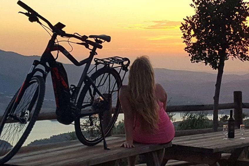 A person sitting on a wooden bench overlooking a sunset, with a bicycle leaning against the bench. 1