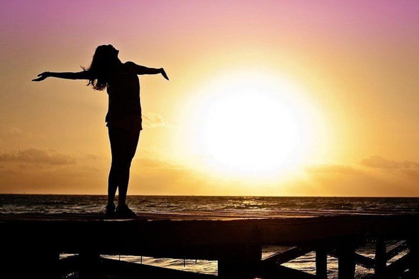 A silhouette of a person with arms outstretched against a sunset on a pier. 1