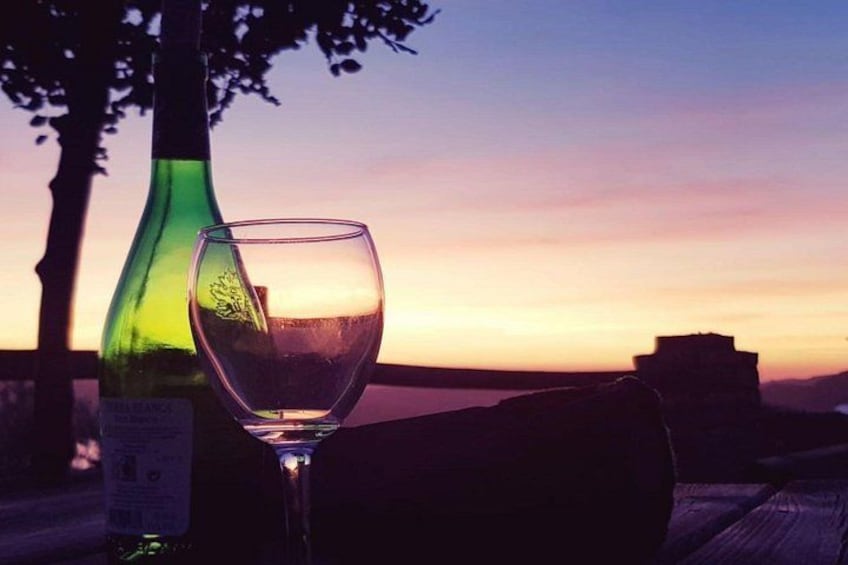 A wine bottle and glass on a wooden surface with a sunset in the background. 4