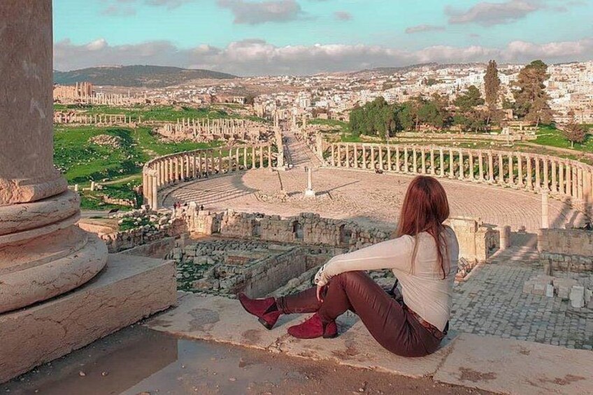 Una persona sentada sobre ruinas antiguas contemplando un paisaje urbano con un coliseo y arcos. 3