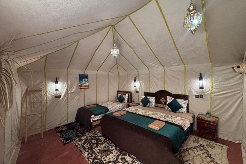 Alojamiento con tiendas de campaña, dos camas, almohadones decorativos, un candelabro y luces montadas en la pared. 4
