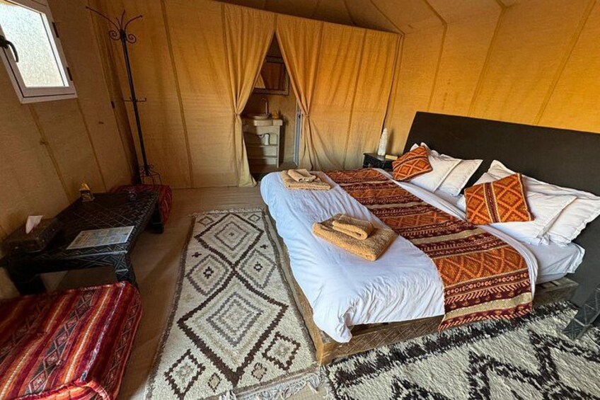 Een tent met twee bedden, een tafel en een kamerkleed met een patroon. 4