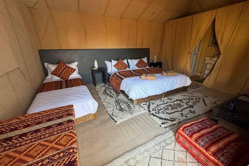 A tented accommodation with two beds, each with patterned bedding, a nightstand, and a rug. 4