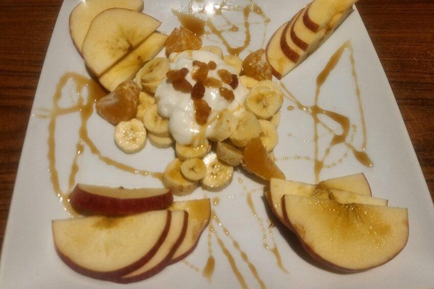 A plate of food with sliced bananas, apples, and a dollop of cream, drizzled with syrup. 2
