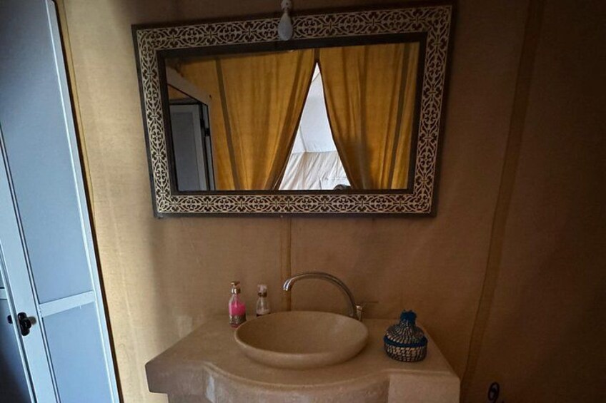A bathroom with a beige sink, a mirror with a decorative frame, and a blue and white bottle on the counter. 5