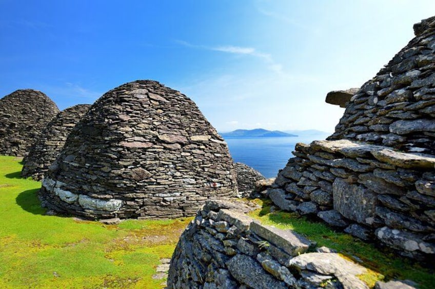Stone structures in a grassy field with a body of water and mountains in the background. 1