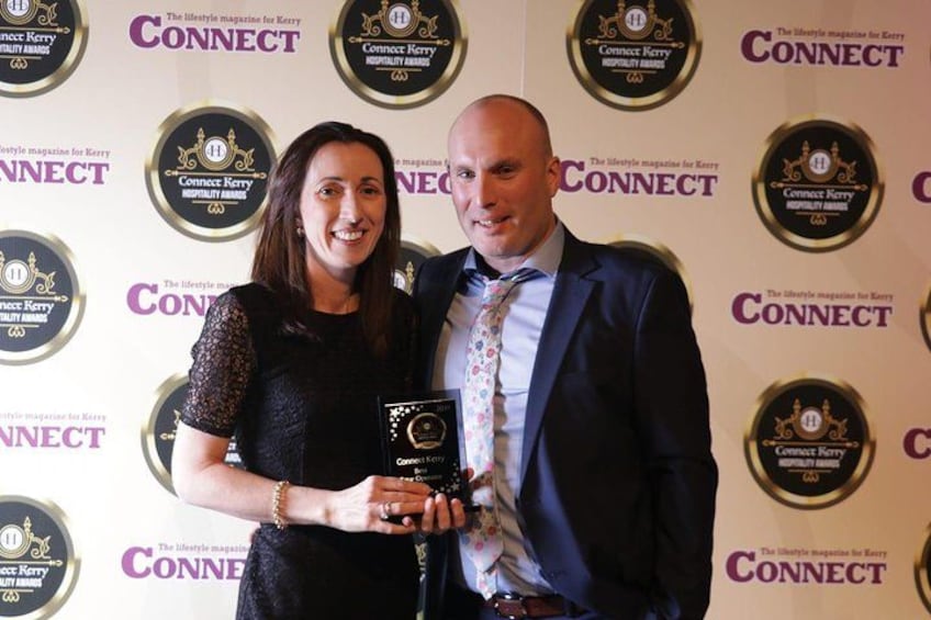 Two people holding an award at an event with a backdrop featuring logos and text. 4