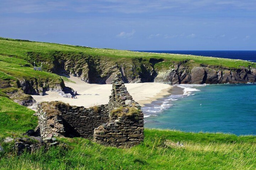 A coastal landscape with a sandy beach, green grass, and a stone structure. 3