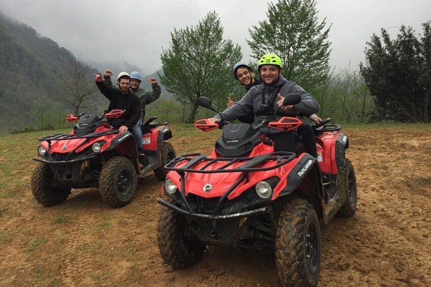 Tres personas en vehículos todo terreno rojos en un campo embarrado, con árboles y montañas al fondo. 4