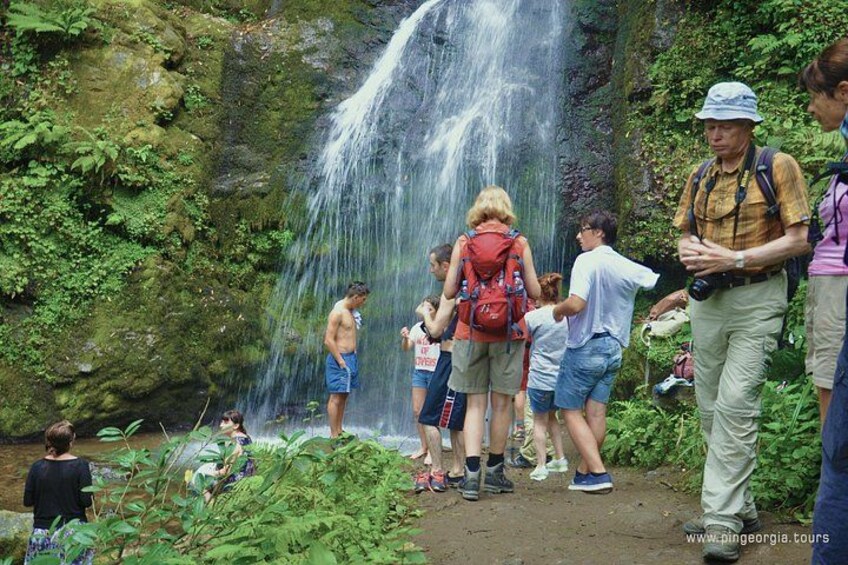 Una cascada con gente de pie a su alrededor, algunas con mochilas. 1