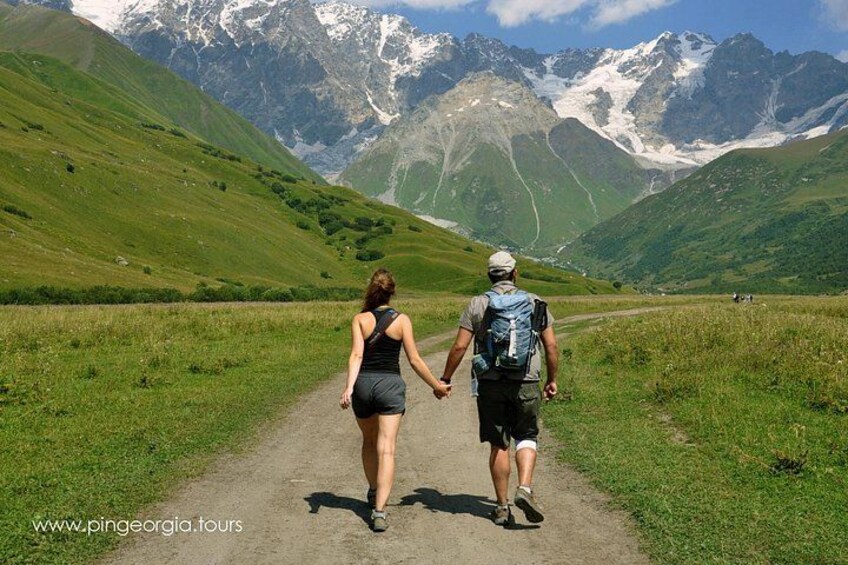 A couple walking on a dirt path with mountains in the background. 1