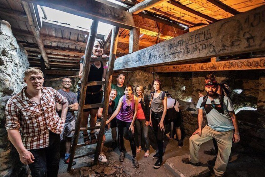 A group of people in a rustic, stone-walled room with wooden beams and a ladder. 3