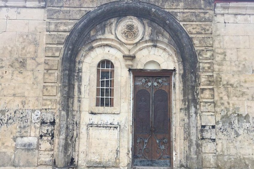 An old stone building with a large arched doorway, a small window, and a decorative emblem above the door. 2