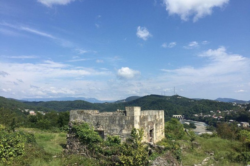 A historical stone structure surrounded by lush greenery and hills in the background. 4