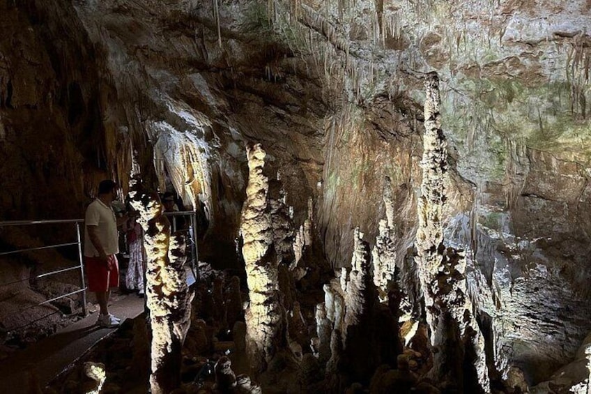 A cave with stalactites and stalagmites, a person standing near a railing, and a cave opening. 3