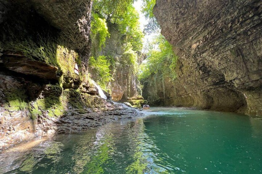 A cave with a turquoise pool, rocky walls, and greenery. 2