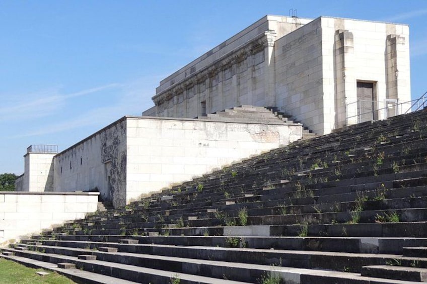 A large, modernist building with a flat roof and a staircase leading up to a platform. 2