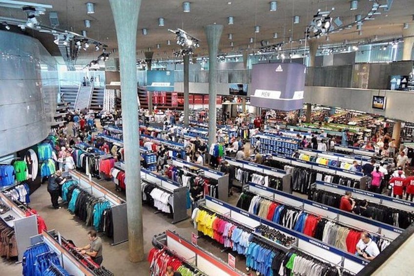 A large indoor retail store with multiple clothing racks and a central staircase. 3