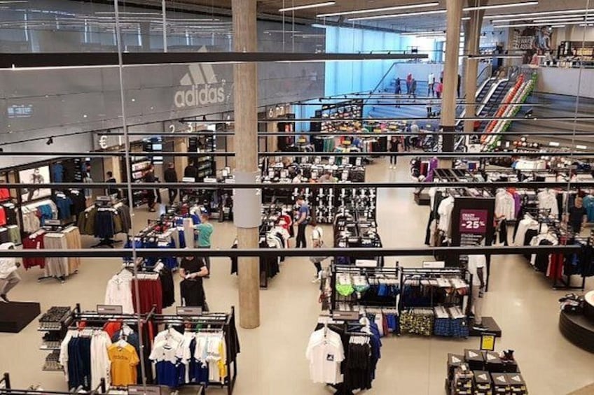 A large indoor shopping mall with multiple levels, clothing stores, and escalators. 2