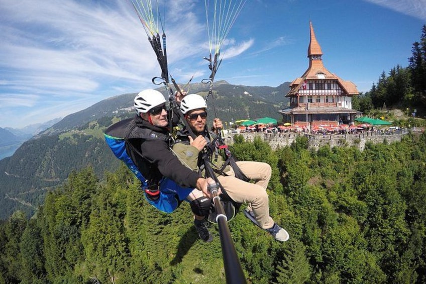 Two people paragliding with a mountain landscape and a traditional building in the background. 2