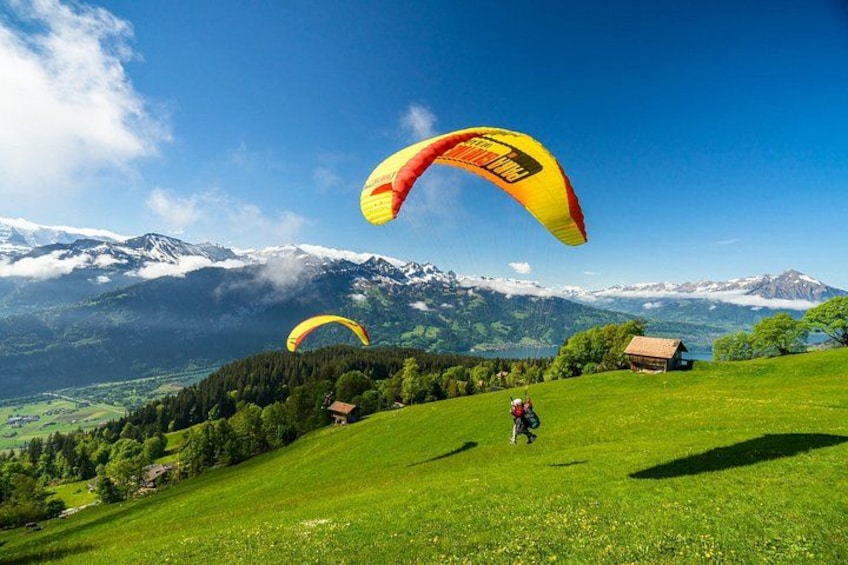 A person paragliding over a grassy hill with mountains in the background. 1