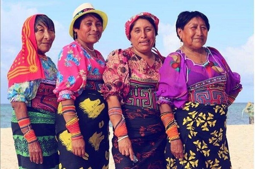 Vier vrouwen in kleurrijke traditionele kleding staan op het strand. 1