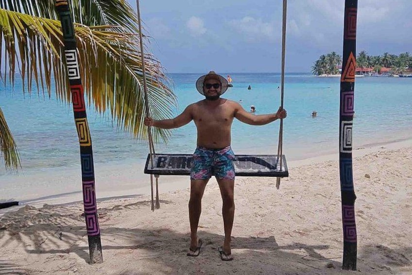 A person on a beach swing with palm trees and a clear blue sea in the background. 5
