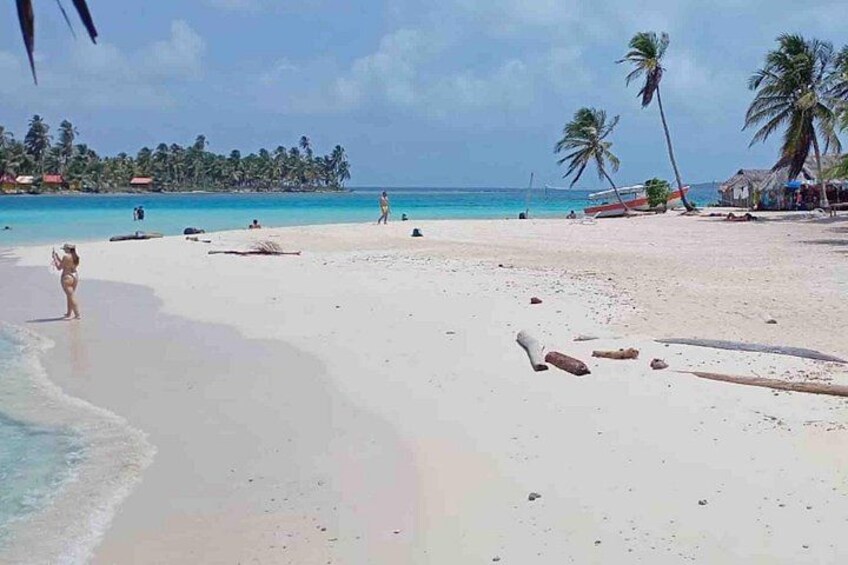 A beach with clear turquoise water, palm trees, and a few people. 4