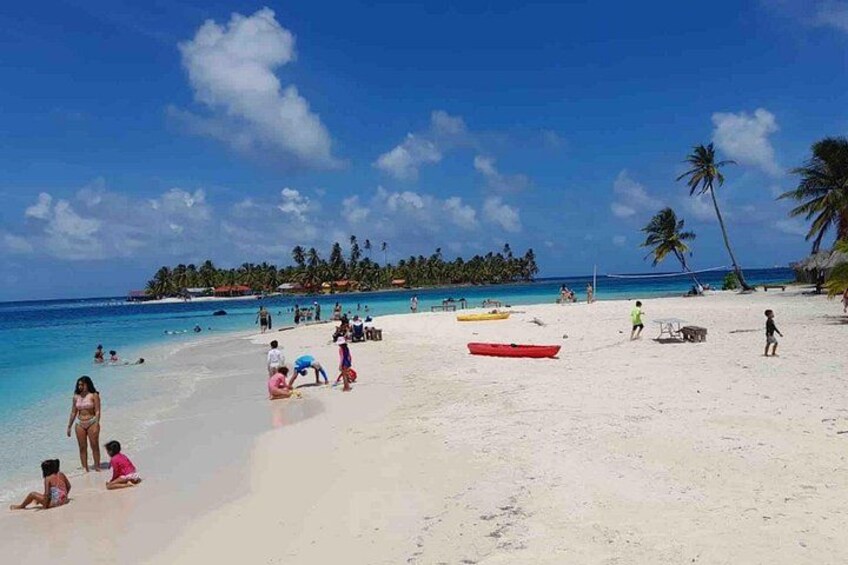 Una playa con gente tomando el sol, un bote rojo y palmeras. 4
