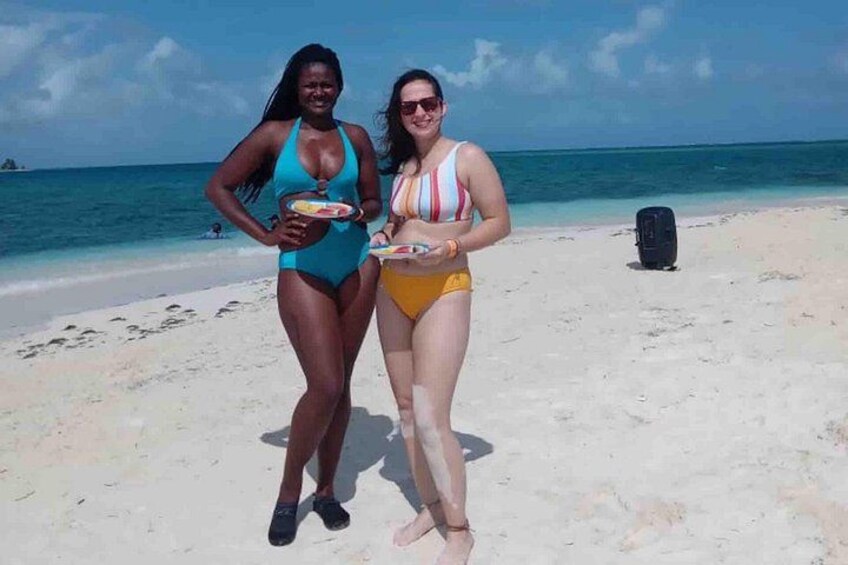 Dos personas en una playa sosteniendo platos con comida, una maleta y un cielo despejado. 5