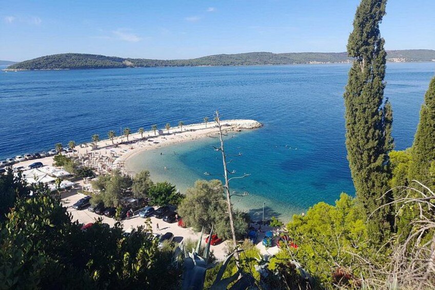 A coastal landscape with a beach, clear blue sea, and a peninsula. 3
