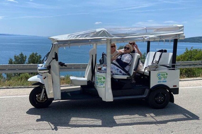 A golf cart with 'etuk city tour' branding parked on a road with a scenic view of the sea and hills in the background. 2
