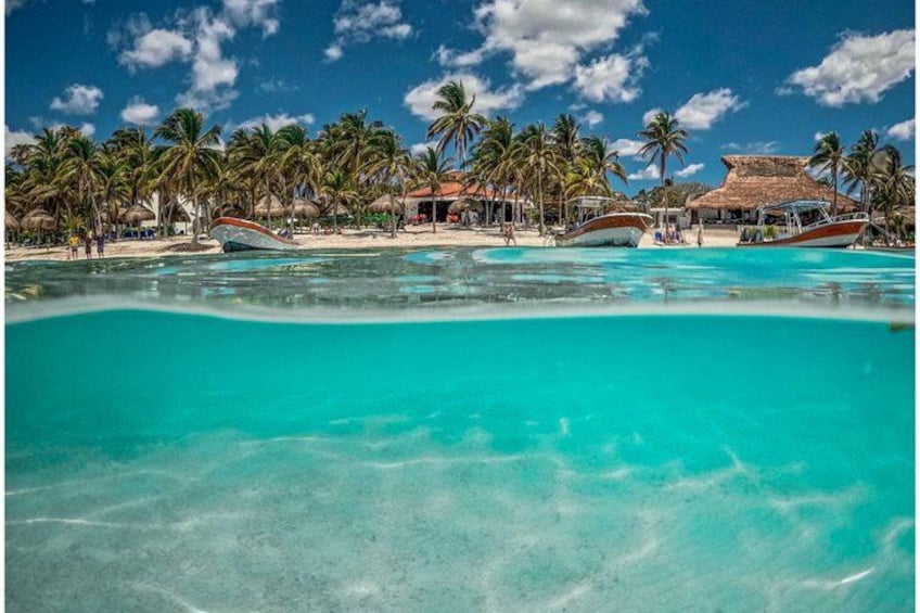 A turquoise lagoon with boats, palm trees, and thatched-roof huts. 3