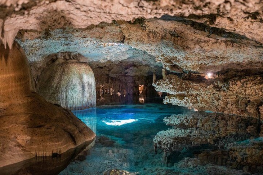 A cave with a pool of water, stalactites, and a wooden structure. 2