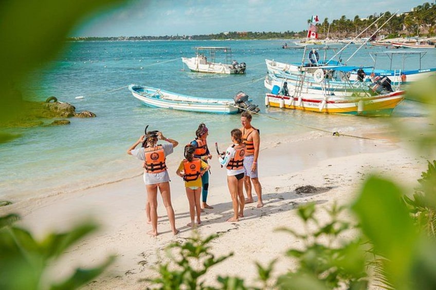 A beach with people wearing life jackets, boats in the water, and a clear sky. 4