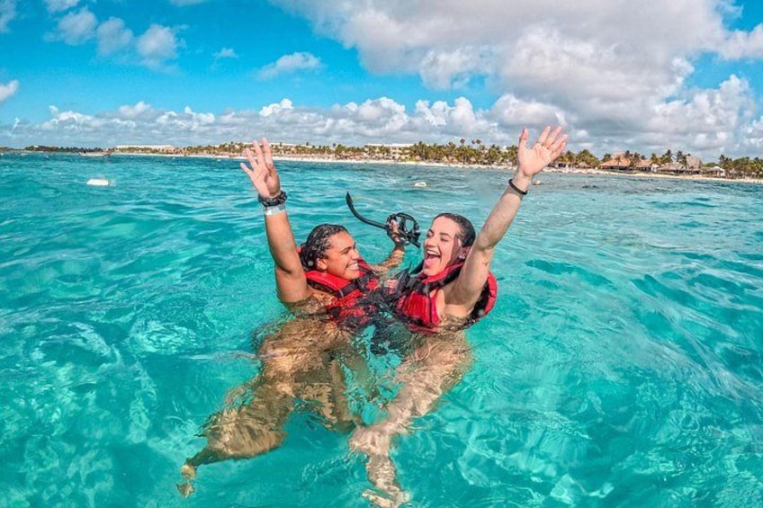Two people snorkeling in clear turquoise water with a tropical beach and palm trees in the background. 3