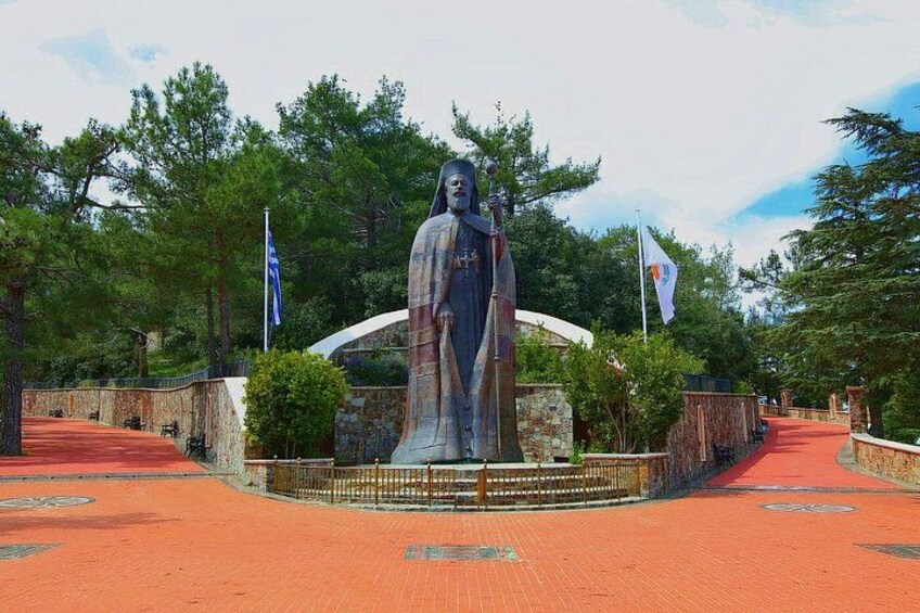 En stor statue i en park med en rød sti, omgivet af træer og flag. 1