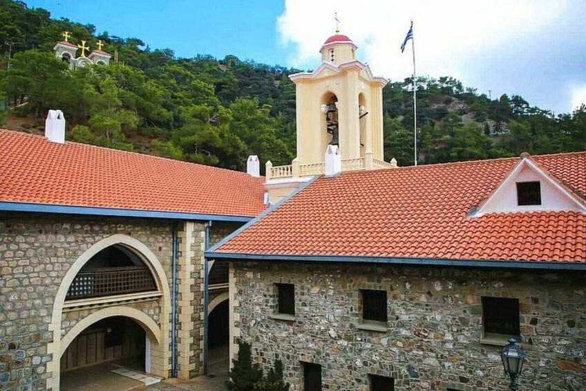 A stone building with a red-tiled roof, a bell tower, and a church with crosses on a hill. 1