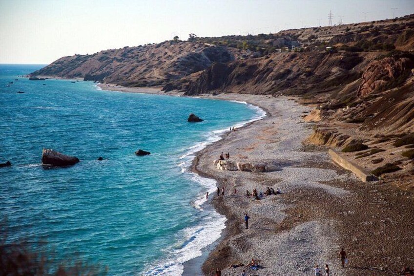 Un paisaje costero con una playa rocosa, aguas azules cristalinas y un terreno montañoso al fondo. 3