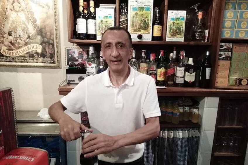 Un homme vêtu d’une chemise blanche coupe une bouteille avec des ciseaux dans un bar. 4