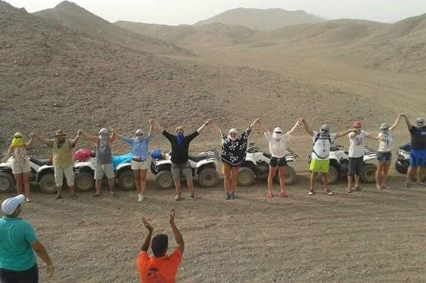 A group of people standing in a line on a dirt road with their arms raised, surrounded by ATVs. 5