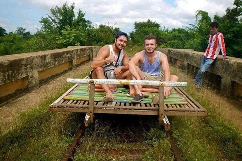 Dos personas sentadas en una plataforma de madera improvisada en una zona con césped, con una estructura de concreto al fondo. 1