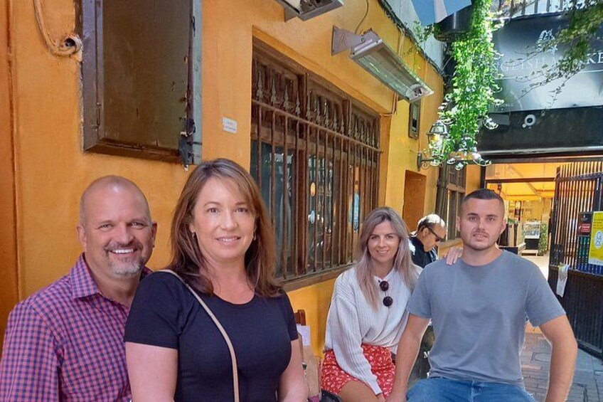 A group of people standing on a street with a yellow building and a black awning in the background. 2