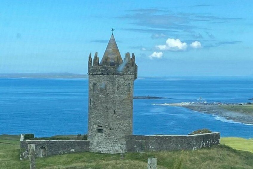 A stone tower with a pointed roof, surrounded by a grassy area and the ocean. 3