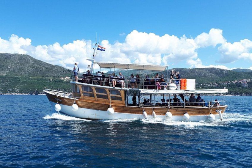 A wooden boat with passengers on a calm sea, surrounded by hills. 5