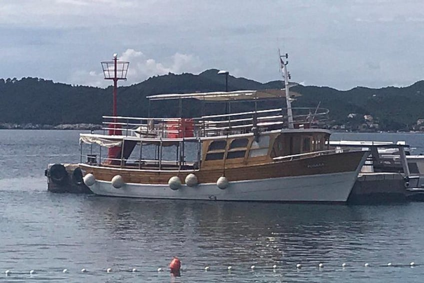 A wooden fishing boat with a cabin, docked at a harbor with calm water and a backdrop of hills. 2