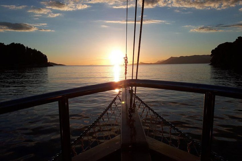 A sunset over water with a boat's bow and a distant shoreline. 1